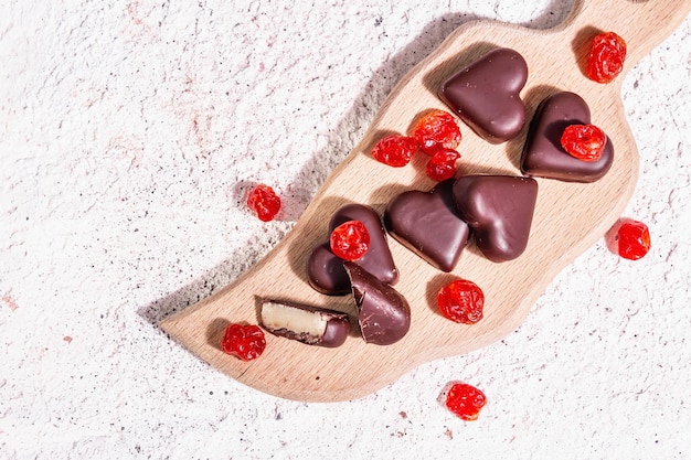 Heart-shaped chocolate candies with dried cherries. Modern hard light, dark shadow. A sweet gift for Valentine's Day or Anniversary. Light tones plaster background, top view