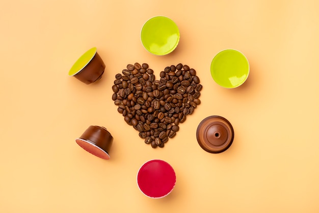 Chicchi e capsule di caffè a forma di cuore intorno sul beige