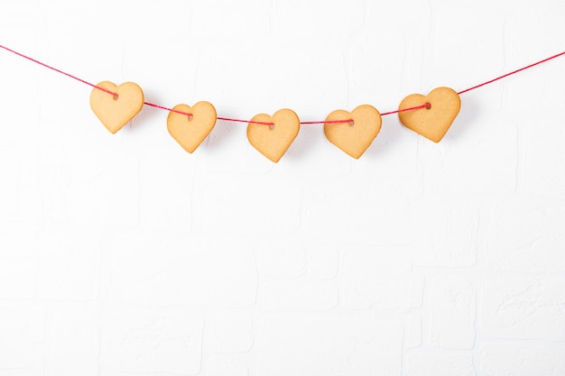 Heart shaped cookies hanging on a white wall. Symbol of cozy love and Valentines Day background and festive concept