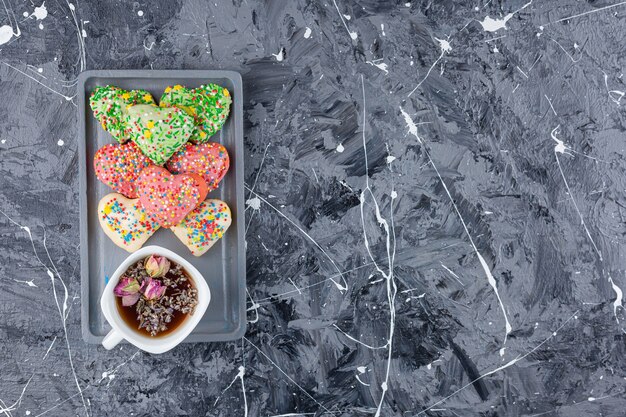 Heart shaped cookies with colorful sprinkles and a cup of black tea . 