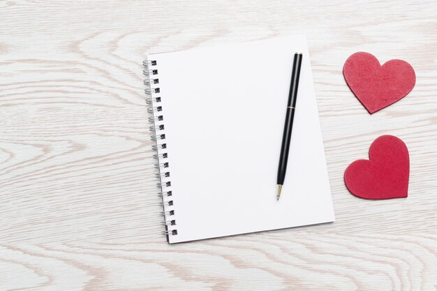 Heart shaped decorations with empty notebook and pen composition for Valentines Day, wooden background with copy space