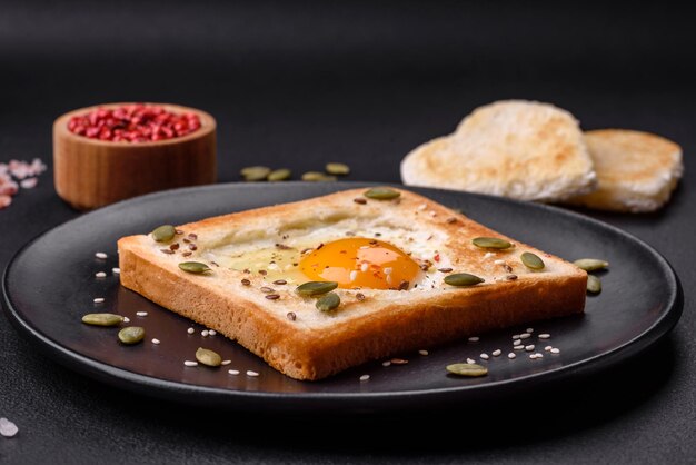 Heart shaped fried egg in bread toast with sesame seeds flax seeds and pumpkin seeds on a black plate