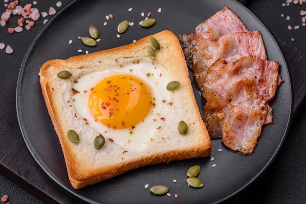 Heart shaped fried egg in bread toast with sesame seeds flax seeds and pumpkin seeds on a black plate