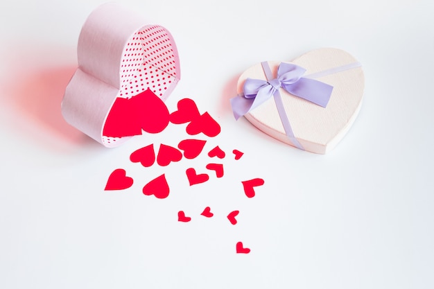 A heart-shaped gift box and red hearts on a pastel background. Valentines day and love shapes background flat lay, top  view