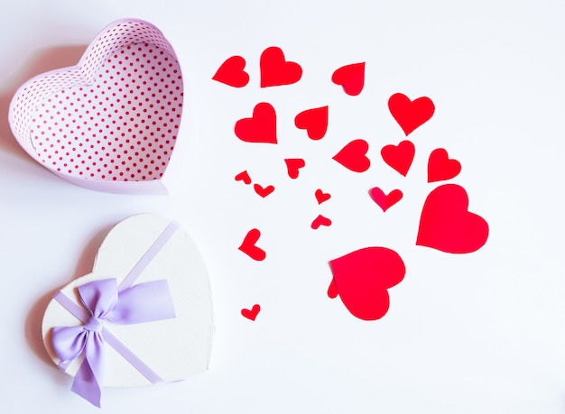 A heart-shaped gift box and red hearts on a pastel background. Valentines day and love shapes background flat lay, top  view