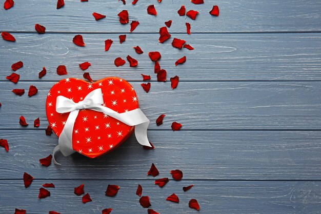 Heart shaped gift box with flower petals on wooden table