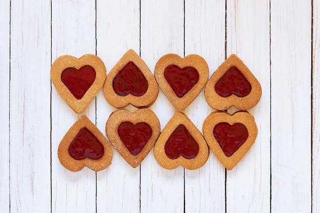 Foto biscotti fatti in casa a forma di cuore con marmellata di fragole su fondo di legno bianco. compleanno, san valentino, festa della mamma. vista dall'alto. biscotti di farina senza glutine