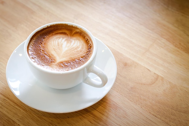 Latte di caffè caldo a forma di cuore in una tazza bianca posta su un pavimento di legno spazio di copia