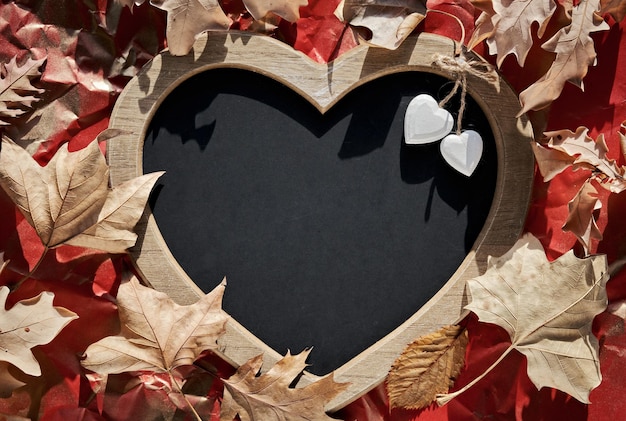 Heart shaped letter board blackboard with heart trinkets Dry Autumn leaves natural Fall decor on crumpled red paper background Copyspace place for your greeting text Flat lay top view