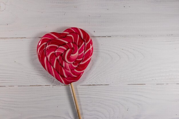 Heart shaped lollipop on white wooden background