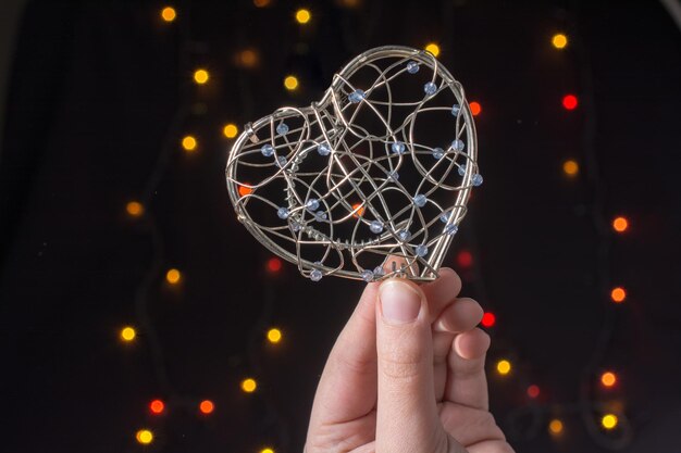 Photo heart shaped metal cage in hand on bokeh light background