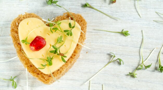 Photo heart shaped mini canapes with butter, cheese and watercress micro greens on a white wooden table. view from above.