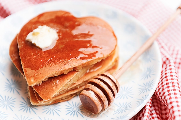 ハート形の明るい背景にパンケーキ。バレンタインデーのお祝いの朝食のコンセプト、または愛する人への楽しいサプライズ