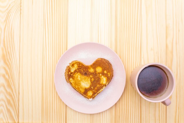 Heart shaped pancakes for romantic breakfast with strawberry jam and black tea