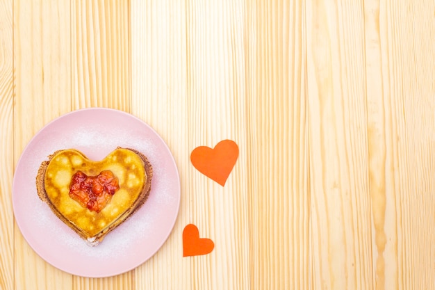 Heart shaped pancakes for romantic breakfast with strawberry jam and paper hearts