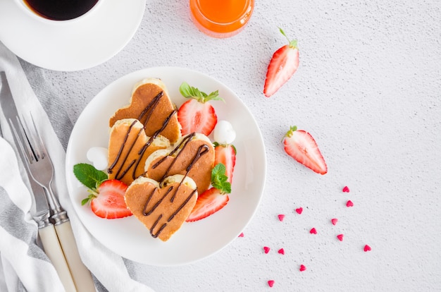 Heart-shaped pancakes with chocolate sauce and fresh strawberries on a white plate