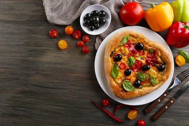 Heart shaped pizza served on plate on wooden background