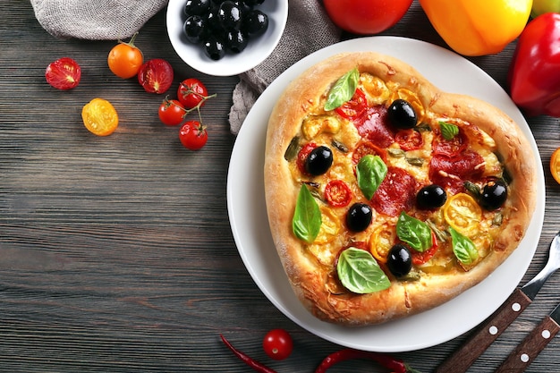 Heart shaped pizza served on plate on wooden background