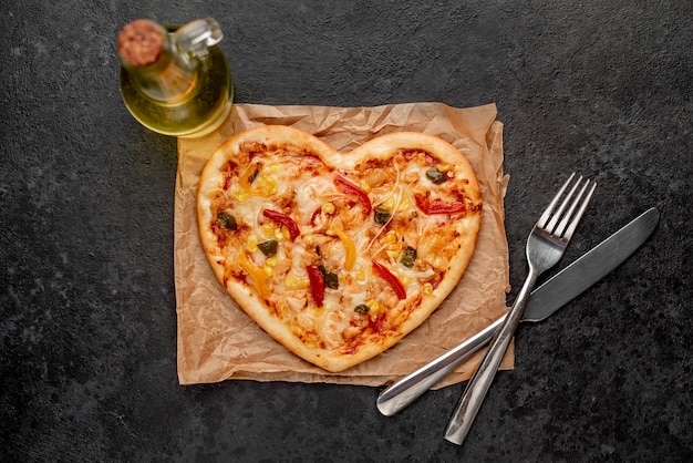 Heart-shaped pizza for Valentines Day with cutlery and olive oil