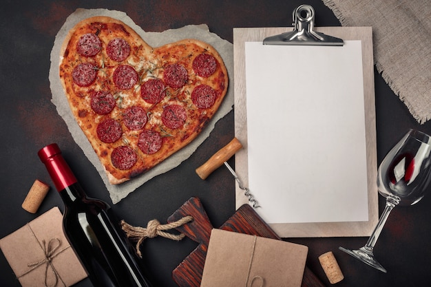 Пицца в форме сердца с моцареллой, колбасой, винной бутылкой, штопором и таблеткой на ржавом фоне