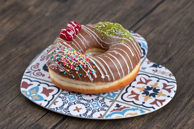 Heart-shaped plate of chocolate donuts decorated with sprinkles and berries on wooden background. 