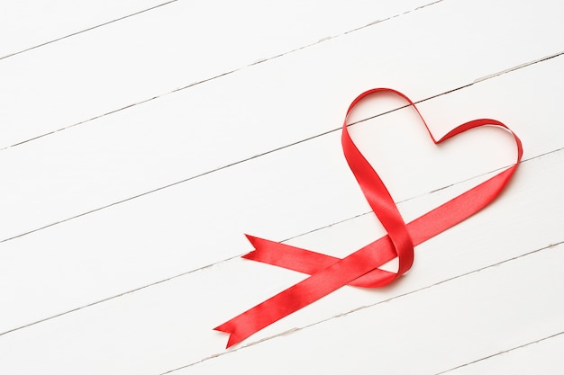 Heart-shaped red ribbon on white wooden background