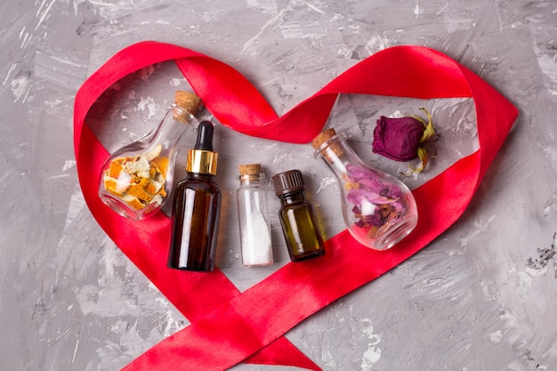  heart shaped red satin ribbon aroma oils bottles, sea salt, dry rose petals and orange peel for scrub