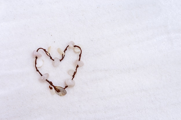 Bracciale a forma di cuore conchiglia sdraiato sulla sabbia fine bianca