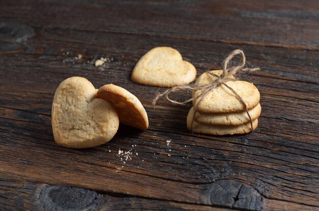 Heart-shaped shortbread cookies tied with a rope and several separate ones located on a dark wooden surface, selective focus