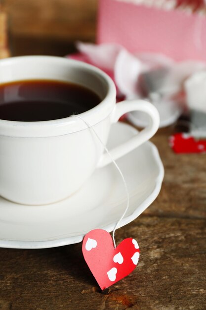 Бирки для чайных пакетиков в форме сердца и чашка чая на деревянном фоне