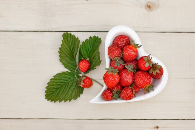 Foto piatto bianco a forma di cuore con fragole su una superficie di legno