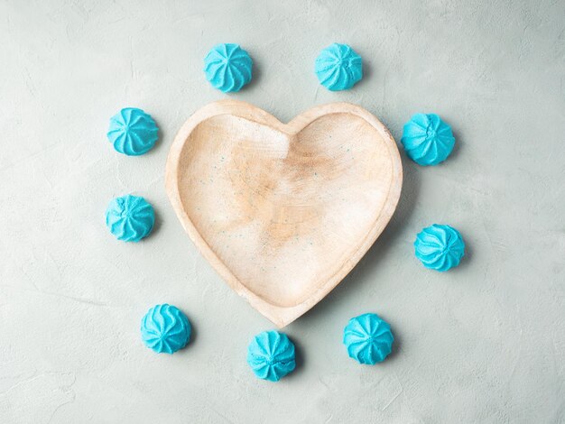 Heart shaped wooden dish with blue sweet meringues flat lay