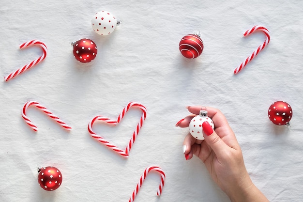 Heart shapes made from candy canes, red and white trinkets with dots on white textile. Hand hold