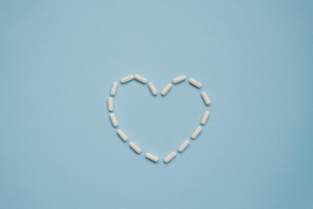 Символ сердца в формате различных таблеток, выделенных на синем фоне, вид сверху Концепция кардиологии и здоровья