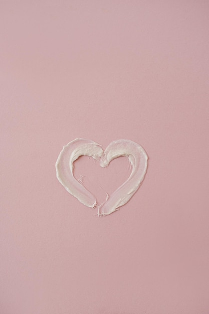 Heart symbol made of cosmetic cream smudge on pink background Aesthetic beauty cosmetic product