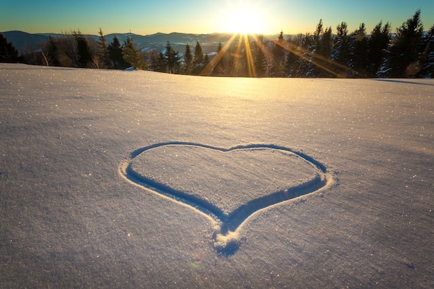 Heart trampled on the snow with feet in a snowdrift on a hillside with a gorgeous view of the coniferous forest and mountain ranges on a sunny frosty day during a ski vacation. Place for text