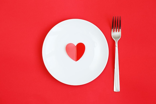 Heart on a white plate with fork on the red background.