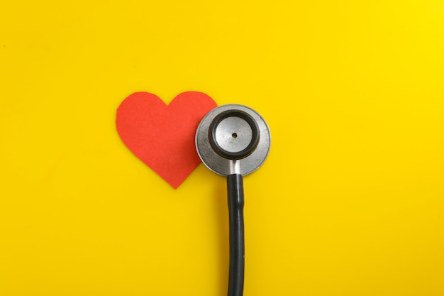 A heart with a stethoscope on yellow background.