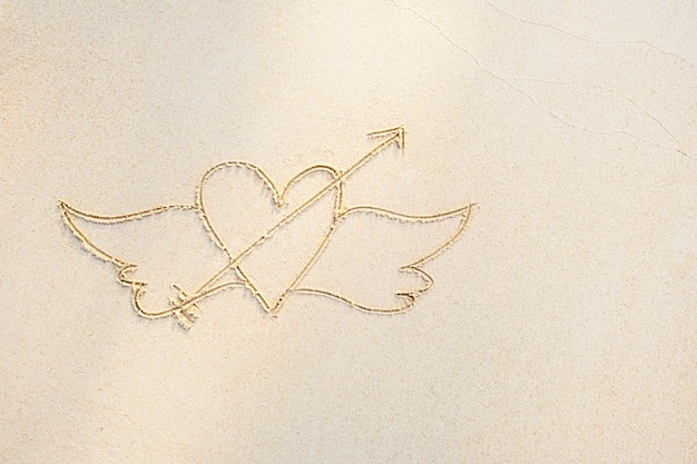 Photo heart with wings drawn on white sand, close up, top view. white sand background, copy space