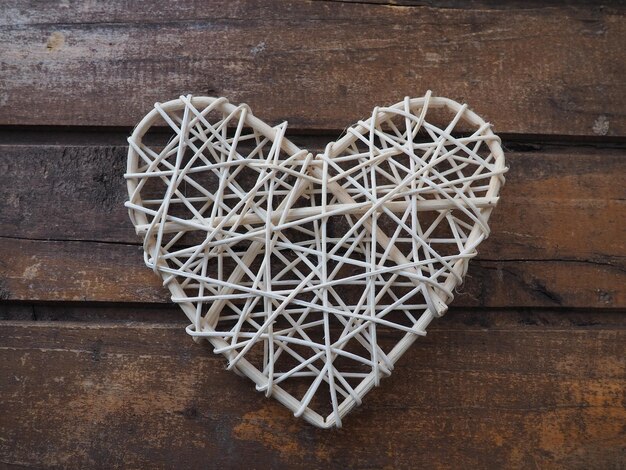 A heart woven from rustic light rods or threads Wicker form handmade Valentine's Day Postcard Wooden texture background Love concept