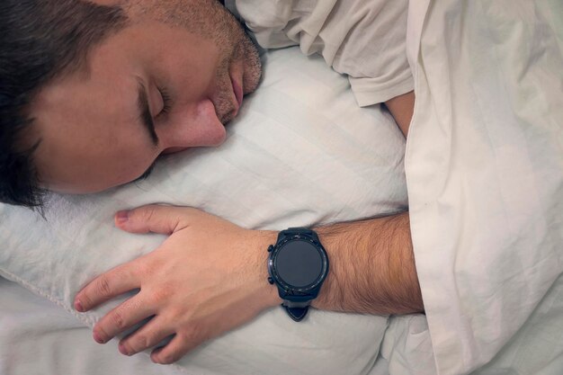 Heartbeat monitoring with a smart gadget in a dream man sleeps on a white pillow with a smartwatch on his wrist to monitor his heartbeat blank screen on the clock blank smartwatch screen