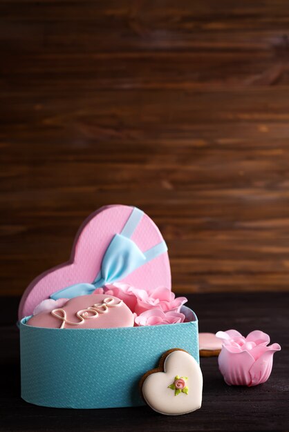 Biscotti dei cuori in scatola blu del cuore con rosa su fondo di legno scuro, spazio della copia