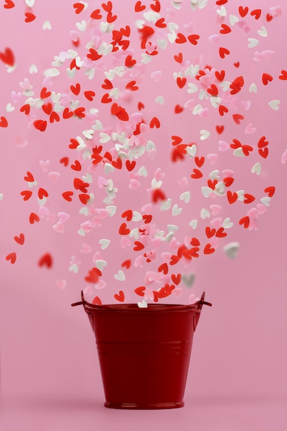 hearts fly out of a red small bucket on a pink background.