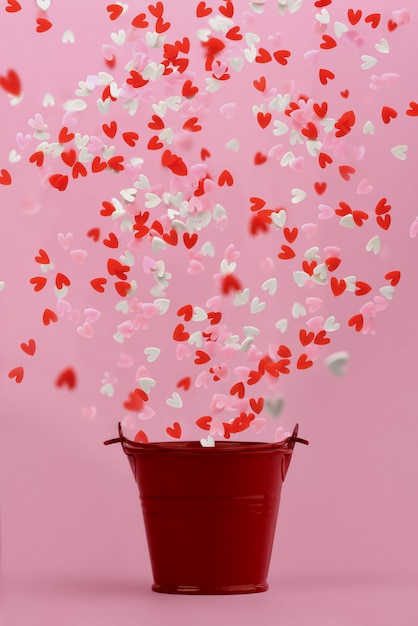 Hearts fly out of a red small bucket on a pink background.