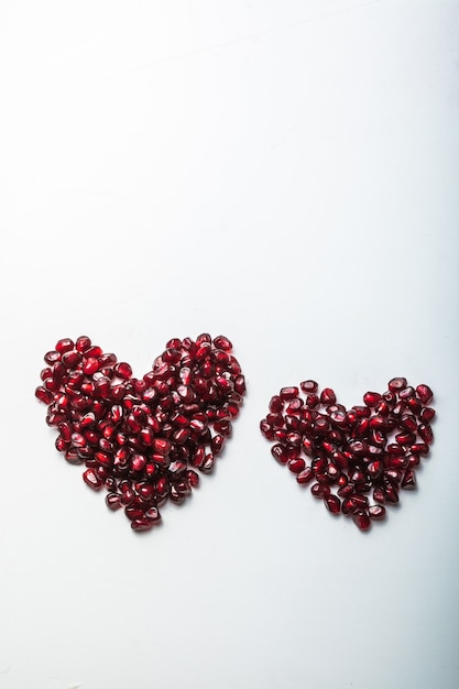 Hearts shape pomegranate seeds on white.