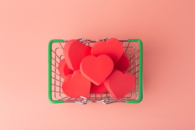 Hearts in shopping cart and supermarket trolley against colored background. background for valentine's day (february 14) and love.