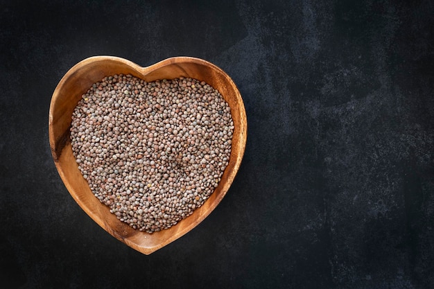 Heartshaped bowl with raw and dried lentils with dark background