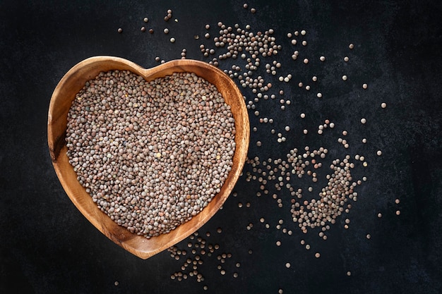 Heartshaped bowl with raw and dried lentils with dark background