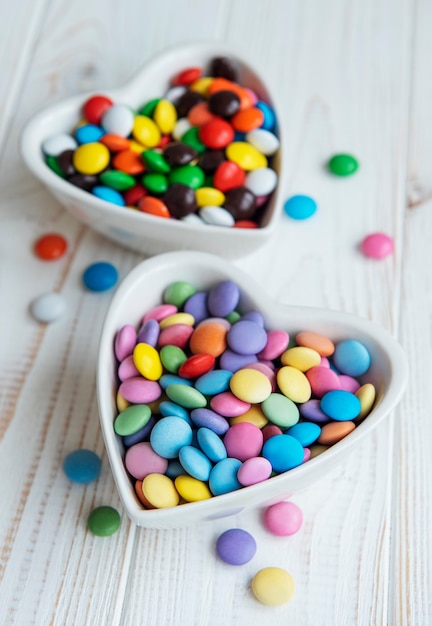 Heartshaped bowls with multicolored dragee sweets on a wooden  surface