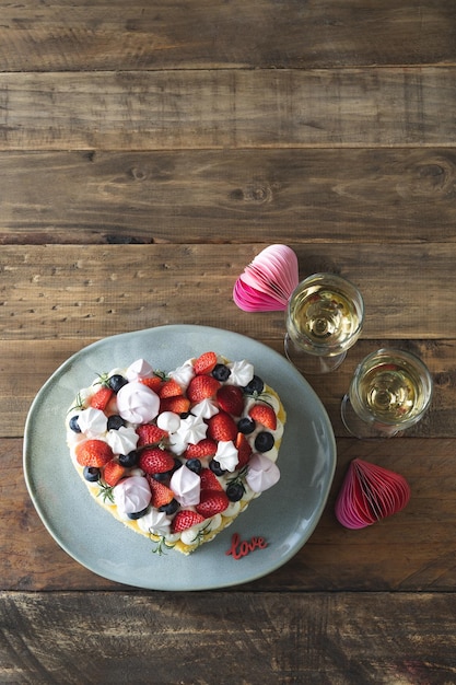 Torta a forma di cuore decorata con frutti rossi e meringa fondo rustico in legno san valentino copia spazio foto verticale